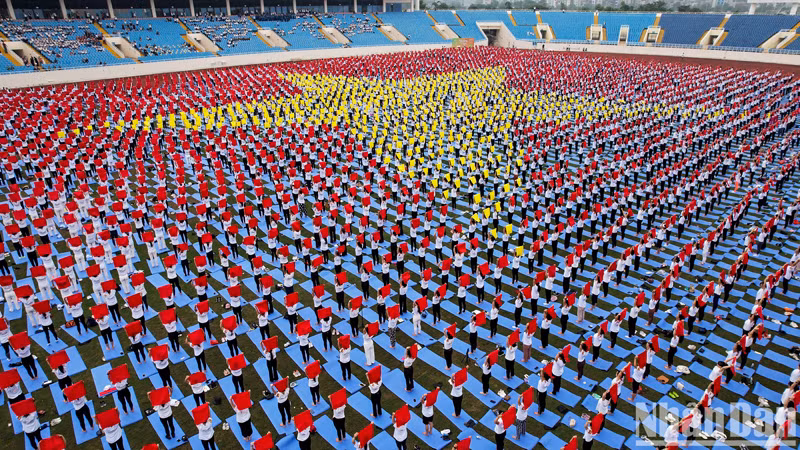 Практикующие йогу двумя руками подняли свои шарфы над головой, образуя форму государственного флага, покрывающего поле стадиона.