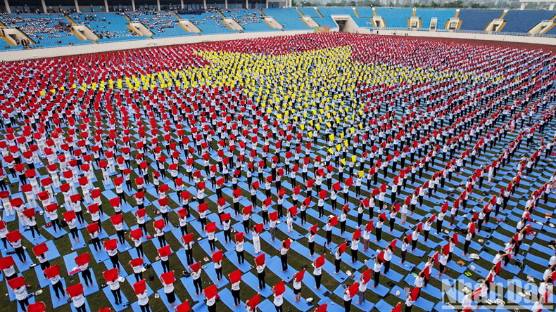 Практикующие йогу двумя руками подняли свои шарфы над головой, образуя форму государственного флага, покрывающего поле стадиона. Практикующие йогу двумя руками подняли свои шарфы над головой, образуя форму государственного флага, покрывающего поле стадиона.